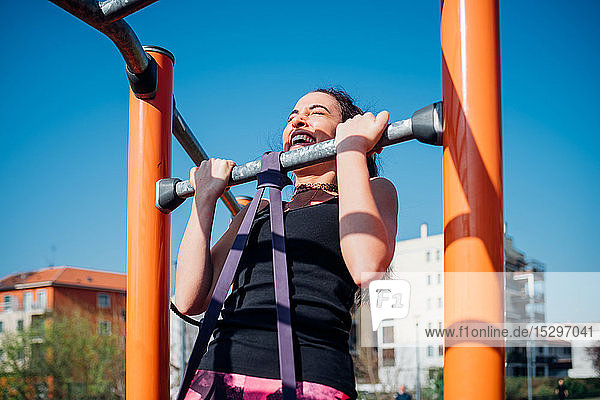 Gymnastik im Fitnessstudio im Freien  junge Frau beim Hochziehen an Fitnessgeräten