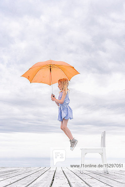 Mädchen wird mit einem Regenschirm von ihrem Stuhl gehoben