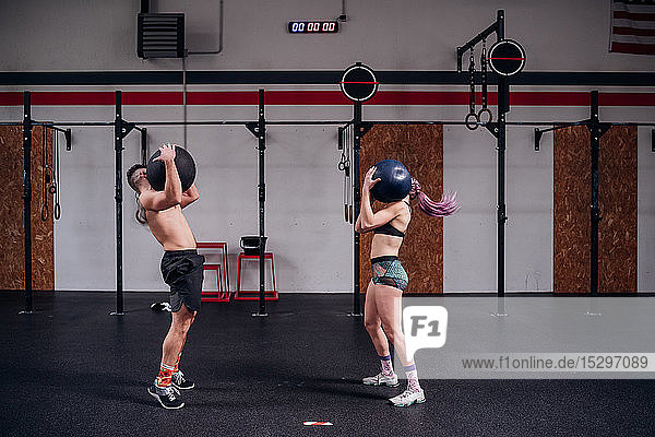 Junge Frau und Mann trainieren zusammen und tragen den Atlasball im Fitnessstudio auf den Schultern