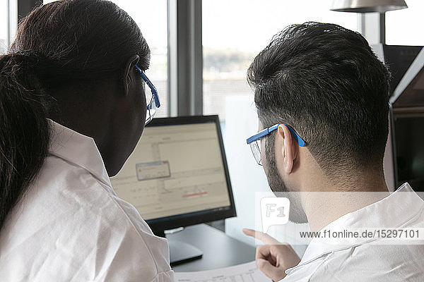 Junge Wissenschaftlerinnen und Wissenschaftler betrachten Papierkram und Computer im Labor Blick über die Schulter