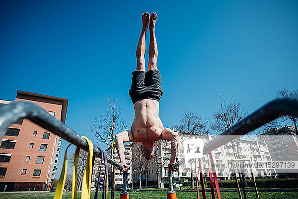 Gymnastik im Freien  junger Mann mit nacktem Oberkörper beim Handstand am Barren  Blickwinkel niedrig