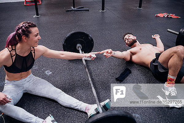 Junge Frau und Mann trainieren zusammen und berühren sich im Fitnessstudio mit den Fingern über der Hantel