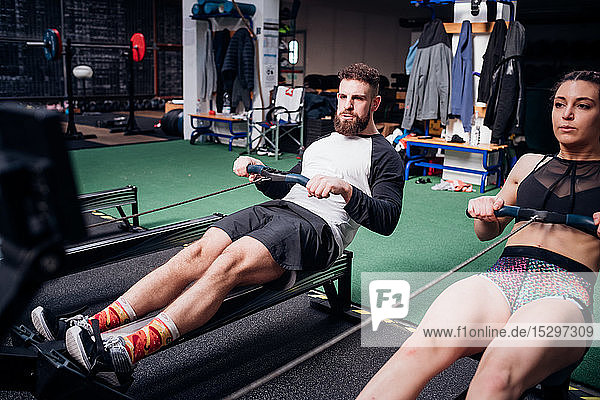 Young woman and man training on rowing machines together in gym