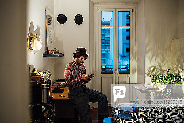 Bearded young man using smartphone on bedroom table