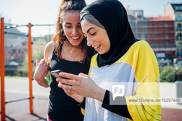 Calisthenics-Kurs im Outdoor-Fitnessstudio  zwei junge Frauen schauen auf ein Smartphone