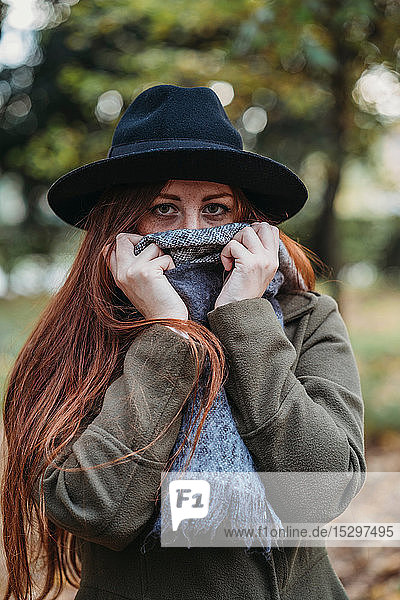 Young woman with long red hair in autumn park covering mouth with scarf  portrait
