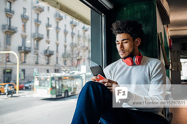 Junger Mann betrachtet Smartphone am Fensterplatz eines Cafés