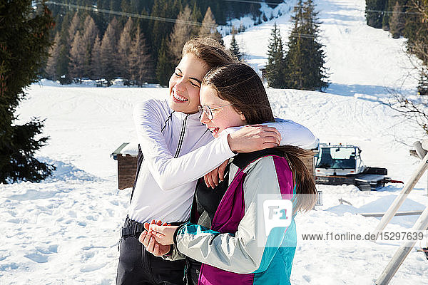Two teenage girl skiers hugging in snow covered landscape  rear view  Tyrol  Styria  Austria