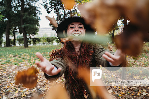 Junge Frau mit langen roten Haaren wirft Herbstblätter im Park