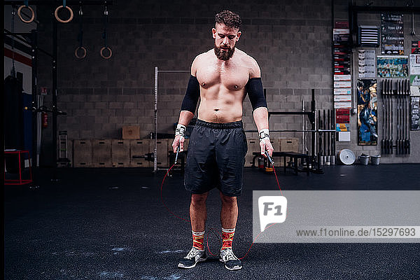 Bare chested young man training  holding skipping rope in gym