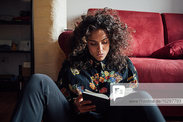 Frau liest Buch  während sie sich ans Sofa lehnt