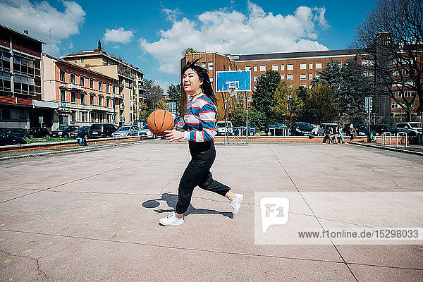 Junge Frau spielt Basketball auf städtischem Basketballfeld
