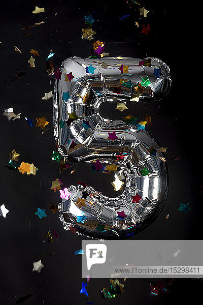Silver balloon and confetti for 5th birthday in front of black background