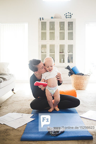 Unternehmerin  die ihre Tochter küsst  während sie zu Hause im Wohnzimmer Yoga praktiziert