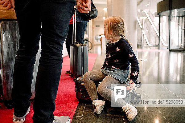 Girl sitting on suitcase with family standing at reception in hotel