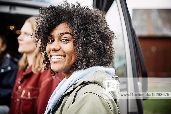 Portrait of smiling young woman with curly hair standing with friend by car