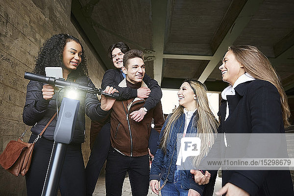 Lächelnde männliche und weibliche Teenager-Freunde mit Elektro-Schieberoller auf dem Fußweg unterhalb der Brücke