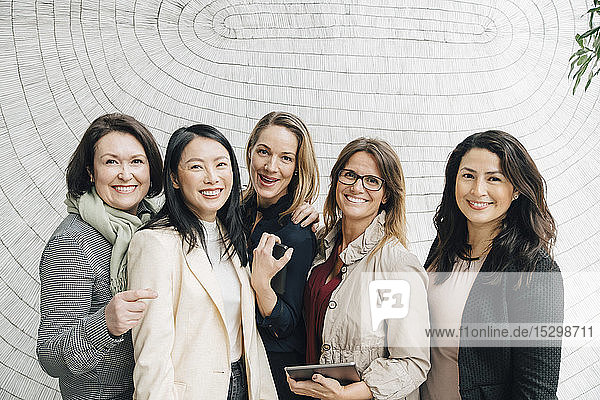 Porträt von lächelnden multiethnischen Unternehmerinnen  die am Arbeitsplatz an der Wand stehen