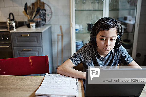 Junge trägt Kopfhörer  während er den Laptop bei den Hausaufgaben zu Hause benutzt