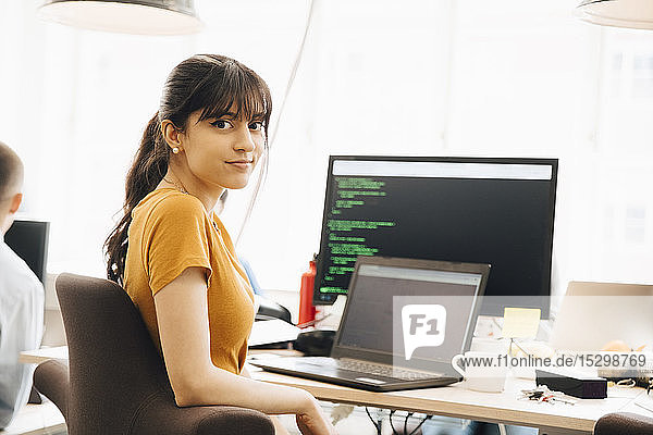 Porträt einer Programmiererin  die im Büro am Schreibtisch sitzt und einen Laptop benutzt