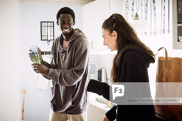 Young man looking at smiling female friend while standing in kitchen at home