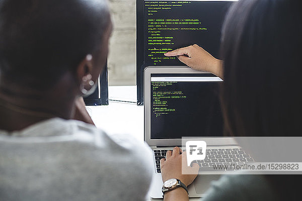 Rückansicht einer Unternehmerin  die auf Codes auf einem Computermonitor zeigt  an einen männlichen Hacker im Büro
