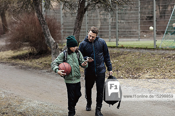 Vater und Sohn benutzen im Winter beim Gehen auf der Straße Mobiltelefone