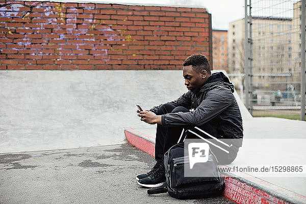 Seitenansicht eines Teenagers  der ein Smartphone benutzt  während er im Winter in der Stadt sitzt