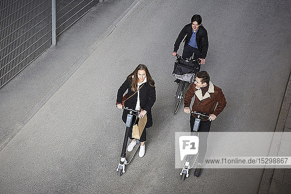 Schrägaufnahme von jugendlichen Freunden auf Elektrorollern und Fahrrädern auf der Straße in der Stadt