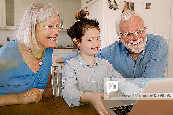 Mädchen zeigt lächelnden Großeltern zu Hause ihren Laptop