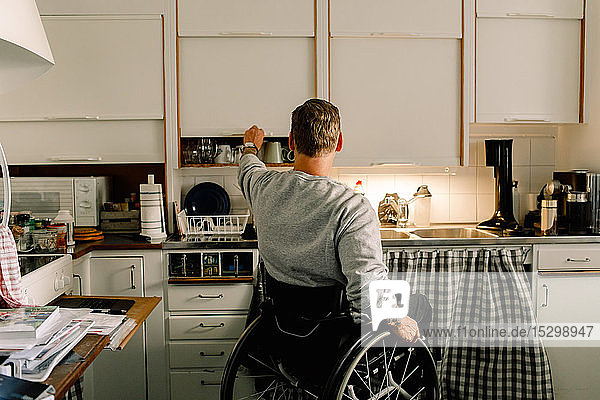 Rückansicht eines behinderten Mannes beim Öffnen eines Schrankes in der heimischen Küche