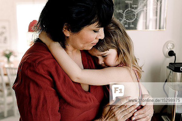 Pflegende Mutter hält traurige Tochter  während sie zu Hause steht