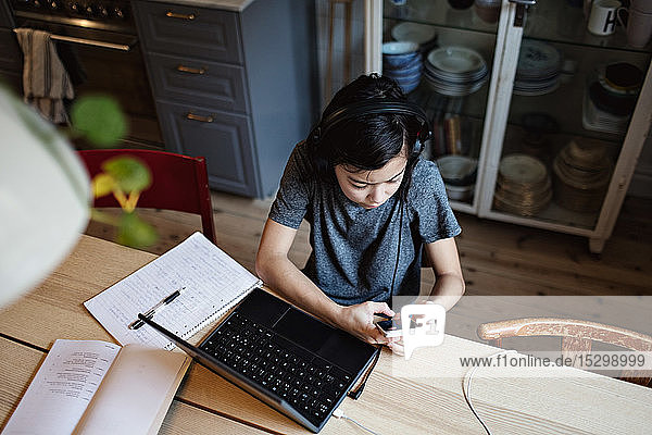 High angle view of studious boy using mobile phone for homework at table