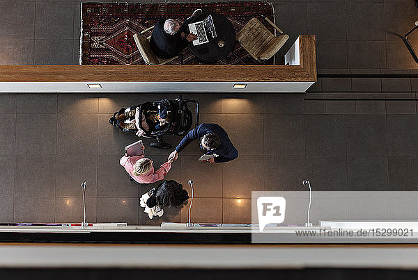 High angle view of businesswoman handshaking male colleague with son while standing in office corridor