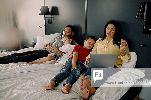 Eltern  die Technologien nutzen  während sie mit Kindern auf dem Bett im Schlafzimmer sitzen