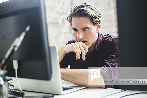 Seriöse männliche IT-Profis denken beim Kodieren am Laptop am kreativen Arbeitsplatz