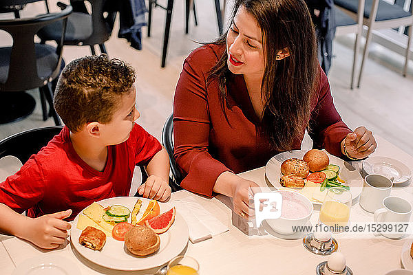 High angle view of mother talking to son while sitting at table in restaurant during breakfast