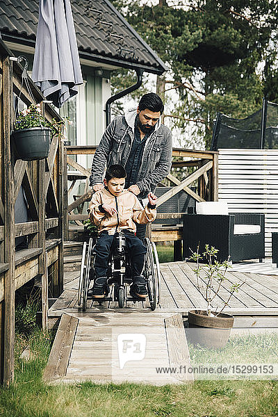 Vater schiebt autistischen Sohn auf Rollstuhl sitzend im Hof
