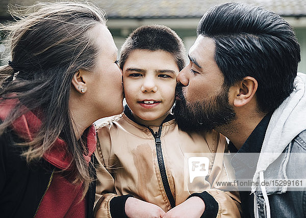 Side view of parents kissing autistic son in yard