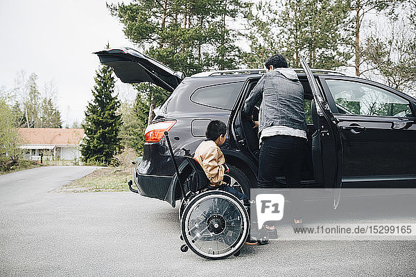 Autistischer Sohn wartet  indem der Vater den Autositz in der Einfahrt verstellt