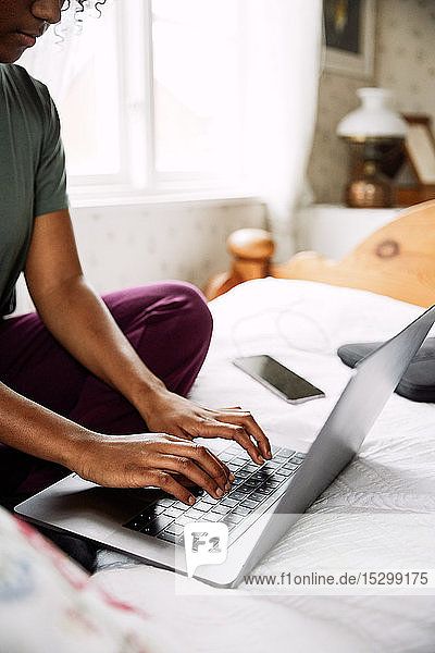 Low section of young woman using laptop while sitting on bed at home