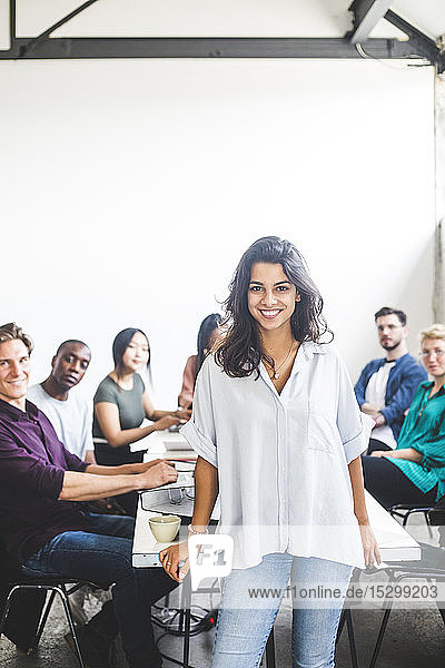 Porträt einer selbstbewussten Programmiererin  die lächelt  während Kollegen im Büro am Konferenztisch sitzen