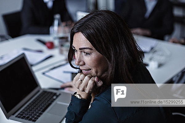 Schrägansicht einer Geschäftsfrau  die mit der Hand am Kinn schaut  während sie am Konferenztisch im Sitzungssaal sitzt