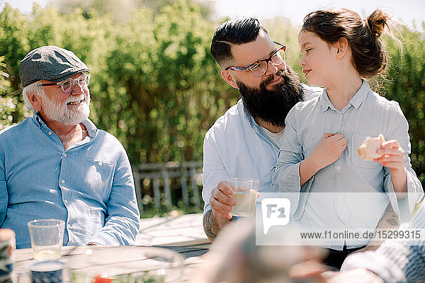Lächelnder älterer Mann betrachtet Familie beim Essen auf der Terrasse