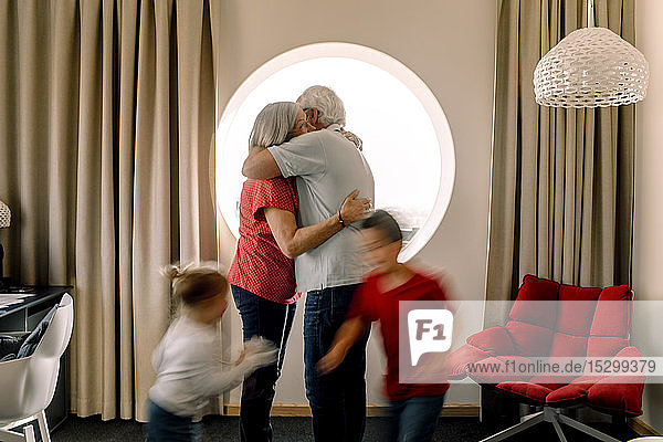 Älteres Ehepaar umarmt sich  während die Enkel im Zimmer spielen