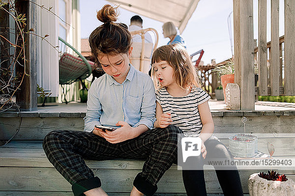 Girl talking to sister using smart phone while sitting on steps in patio