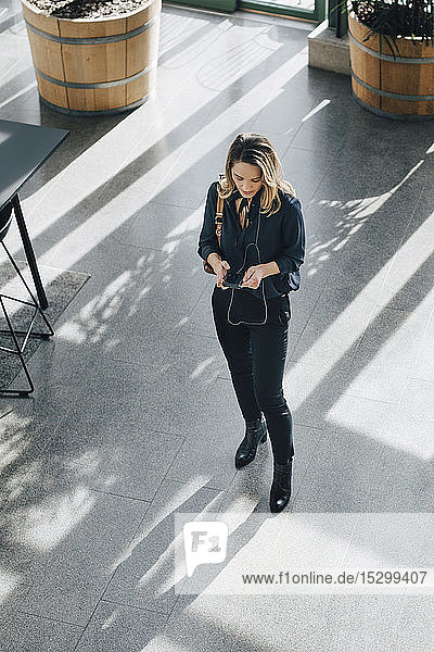 Geschäftsfrau in voller Länge mit Smartphone im Stehen im Büro