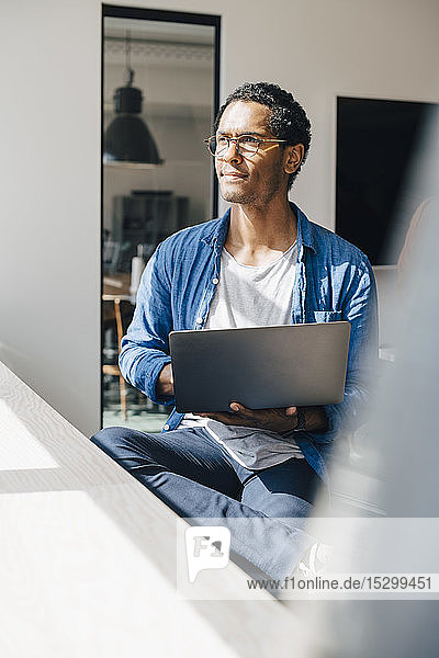Computer programmer with laptop looking away while sitting in office