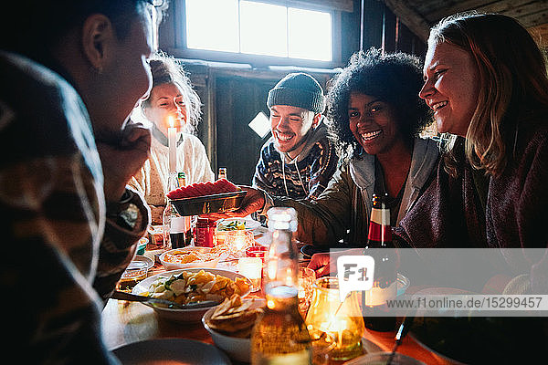 Männliche und weibliche Freunde unterhalten sich beim Essen auf dem Tisch im Blockhaus