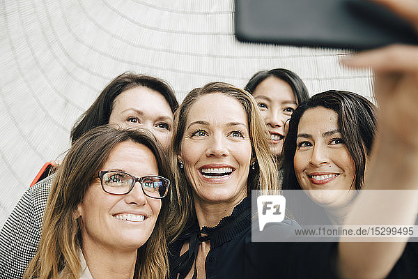 Smiling businesswoman taking selfie with female professionals at office during conference event